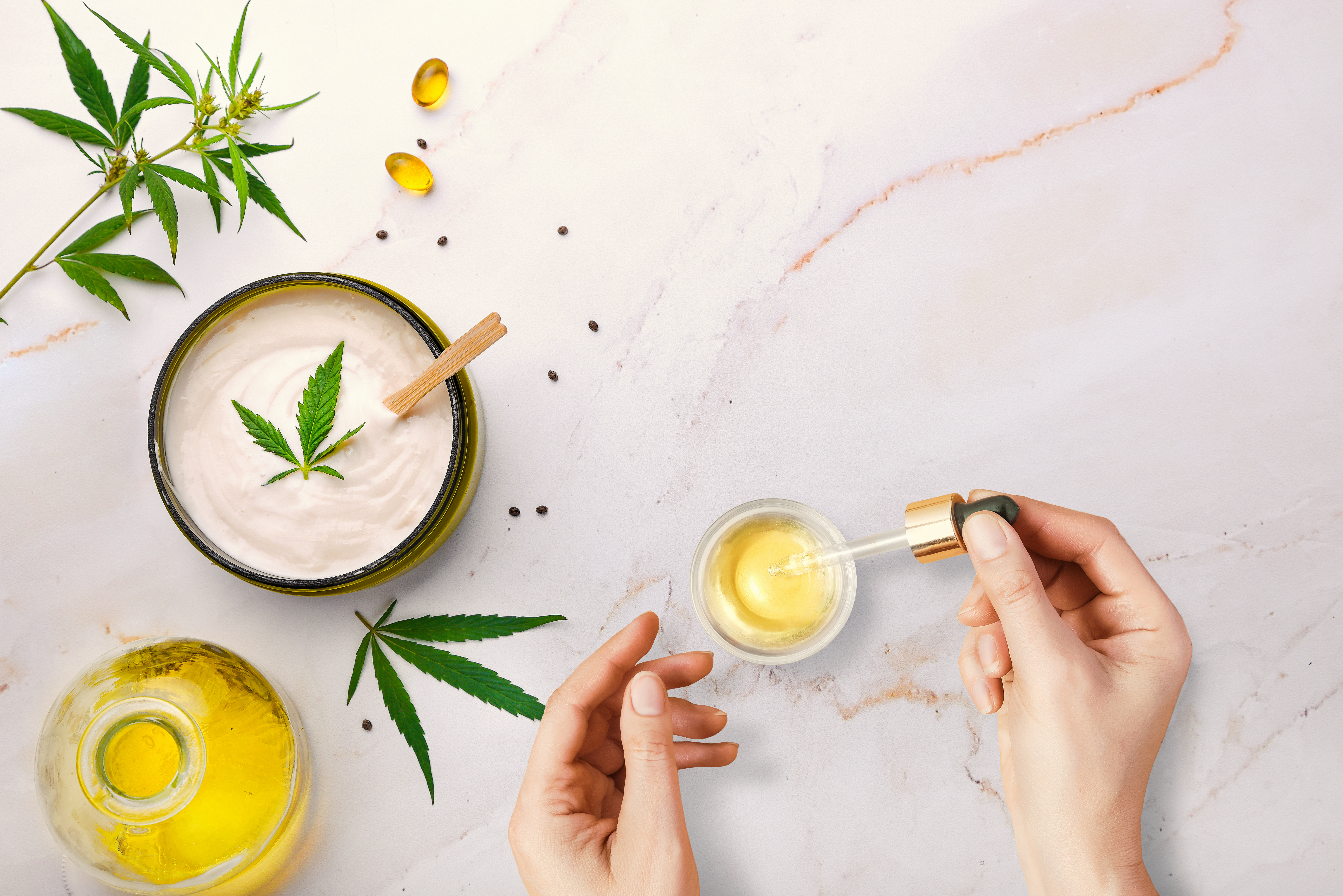 CBd Oil Pipette with CBD cosmetic oil in female hands on a table background with cosmetics, cream with cannabis and hemp leaves, marijuana.