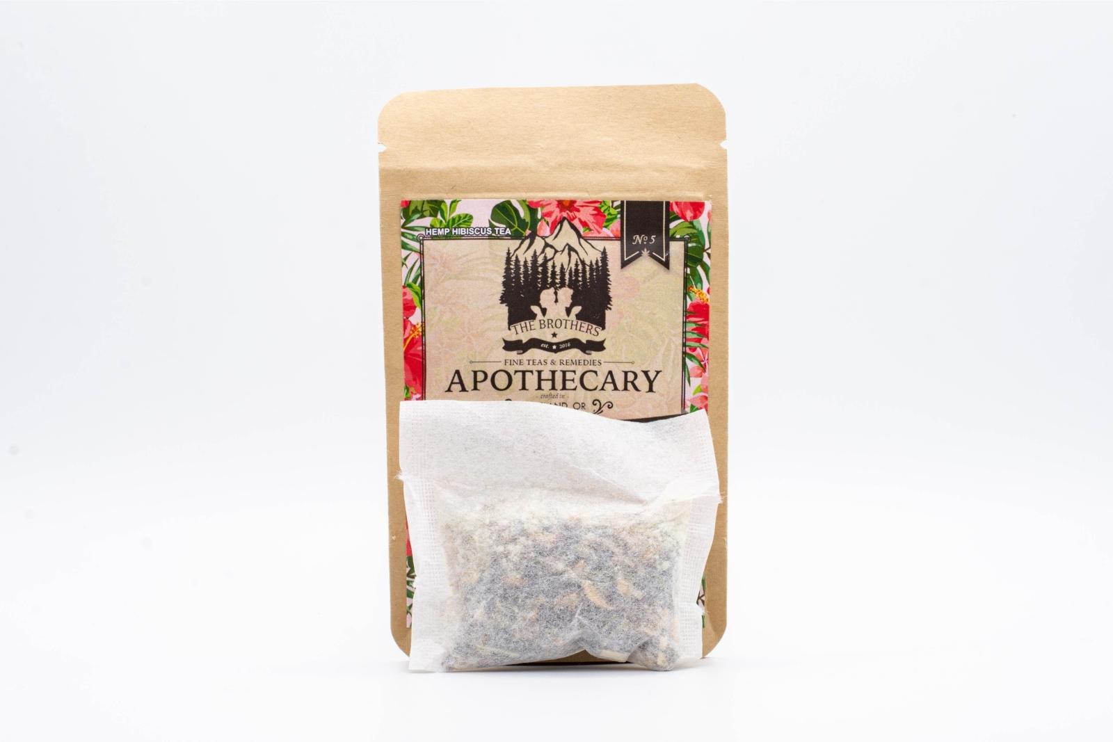 A tea bag in front of a small packet of The Brothers Apothecary's Highbiscus Tea on a white background