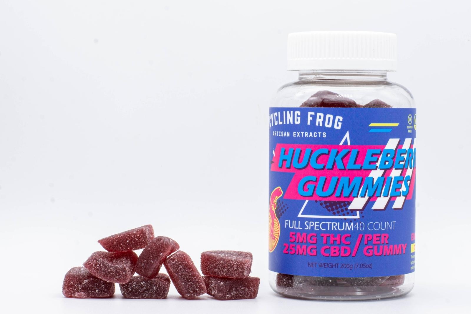 One 40-count Huckleberry CBD gummies by Cycling Frog, next to a pile of the gummies, on a white background
