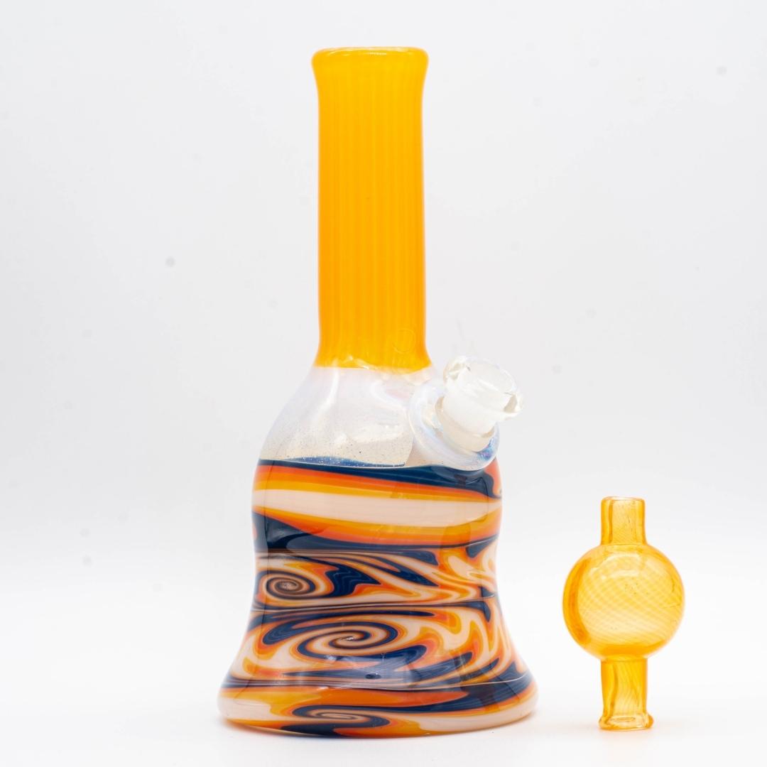 A tangie 6-inch glass rig, next to its bubble cap, made by Bradfurd Glass, on a white background