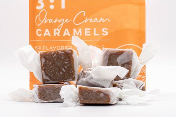 A bag of 3:1 Orange Cream Caramels by Seventh Hill CBD, next to a pile of the caramels, on a white background