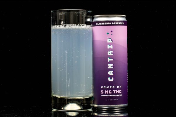 A single can of blackberry lavender flavored hemp infused seltzer by Cantrip, next to a clear glass container displaying the drink, on a black background