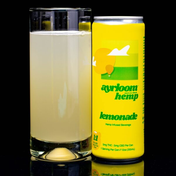 A single can of hemp infused lemonade by ayrloom hemp, next to a clear glass container containing the drink, on a black background