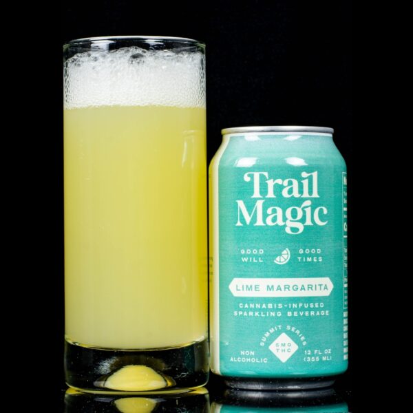 A single can of Lime Margarita infused sparkling beverage, by Trail Magic, next to a clear glass container containing the drink, on a black background