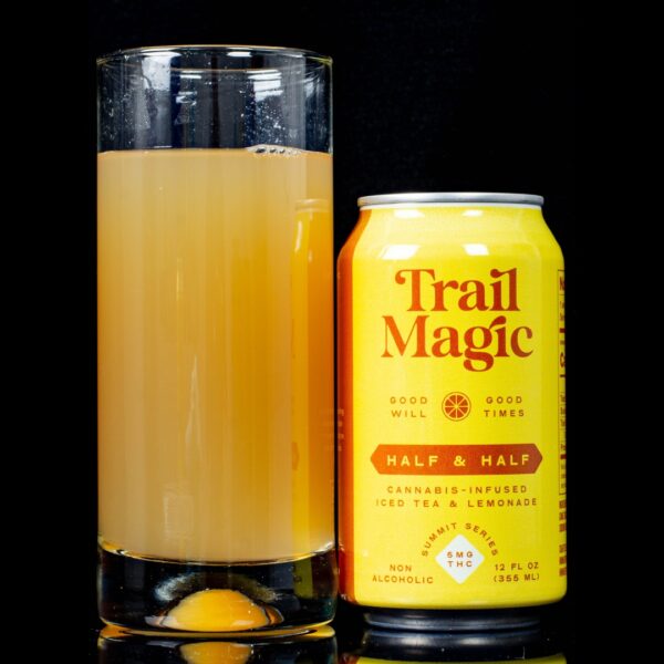 A single can of Half & Half infused sparkling beverage, by Trail Magic, next to a clear glass container containing the drink, on a black background