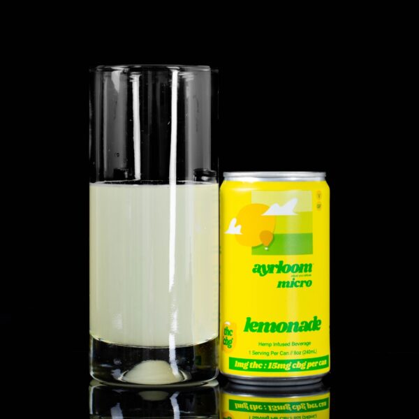 A single can of Lemonade Ayrloom Micro Infused Beverage next to a clear glass container containing the drink, on a black background