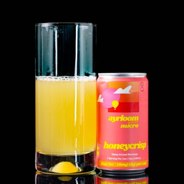 A single can of Honeycrisp Ayrloom Micro Infused Beverage next to a clear glass container containing the drink, on a black background