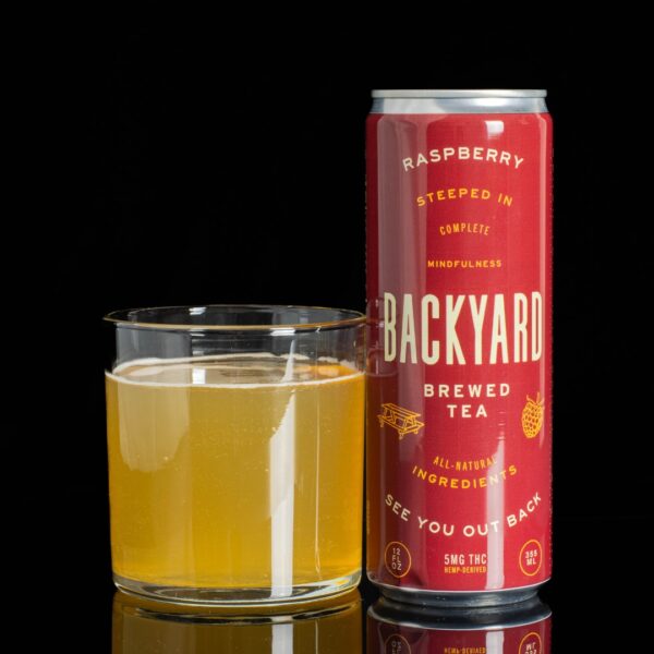 A single can of Raspberry flavored Backyard Infused Tea, next to a clear glass container containing the drink, on a black background