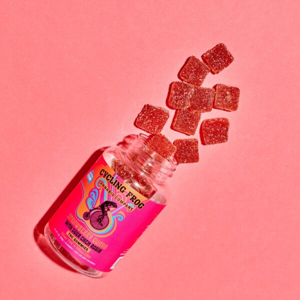 An overhead shot of a spilled over Cycling Frog Strawberry Guava gummies showing the gummies spilling out of the jar. Everything is on a pink background.