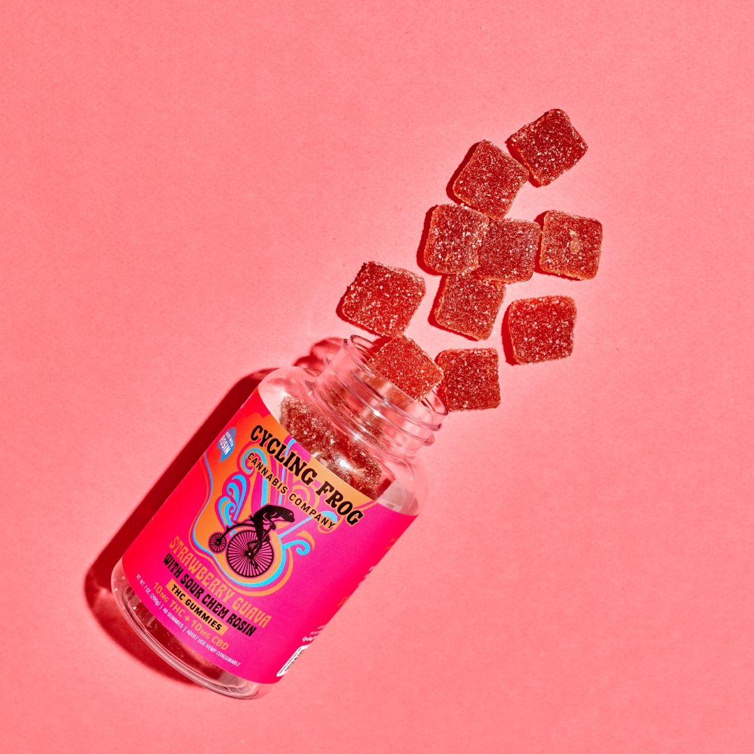 An overhead shot of a spilled over Cycling Frog Strawberry Guava gummies showing the gummies spilling out of the jar. Everything is on a pink background.